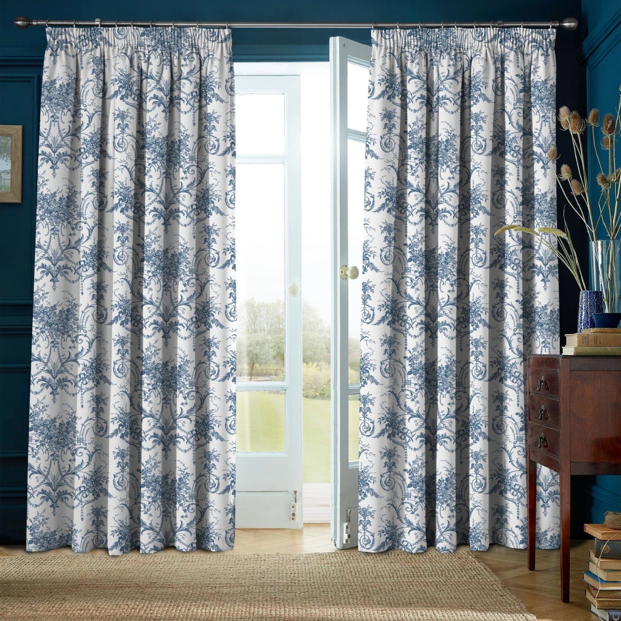 Pair of blue and white floral curtains in a room with a blue wall and wooden floor.