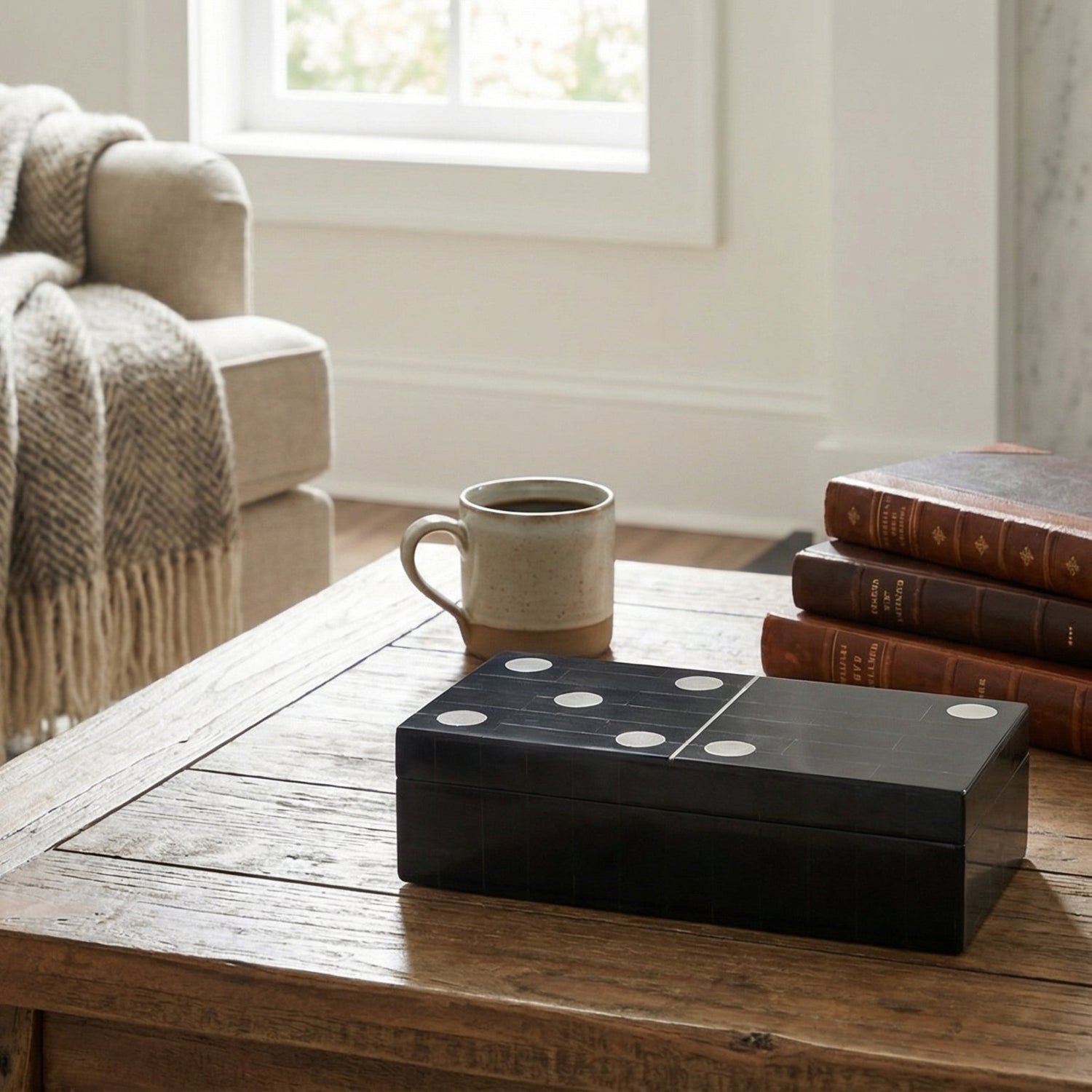 Black box on a wooden coffee table in a cozy living room with books and a mug.