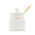 White ceramic honey jar with a wooden dipper on a white background