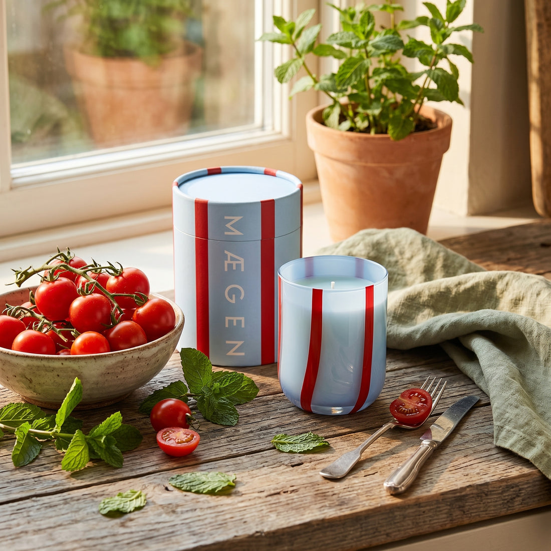 Candle with striped design on a wooden surface with tomatoes and mint in the background
