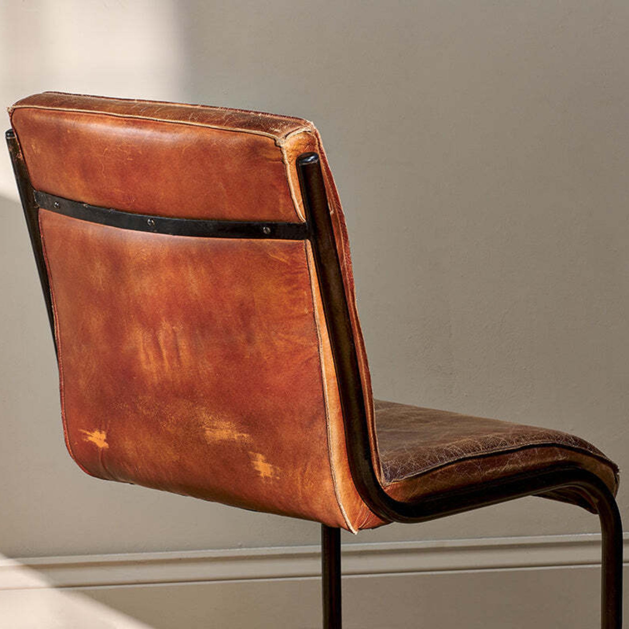 Brown leather chair with metal frame against a neutral wall