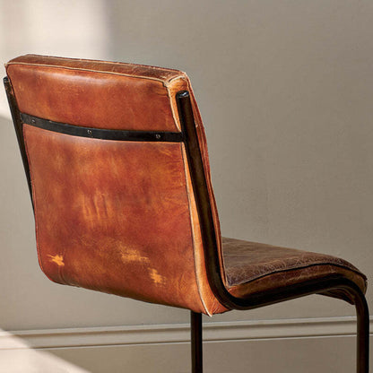 Brown leather chair with metal frame against a neutral wall