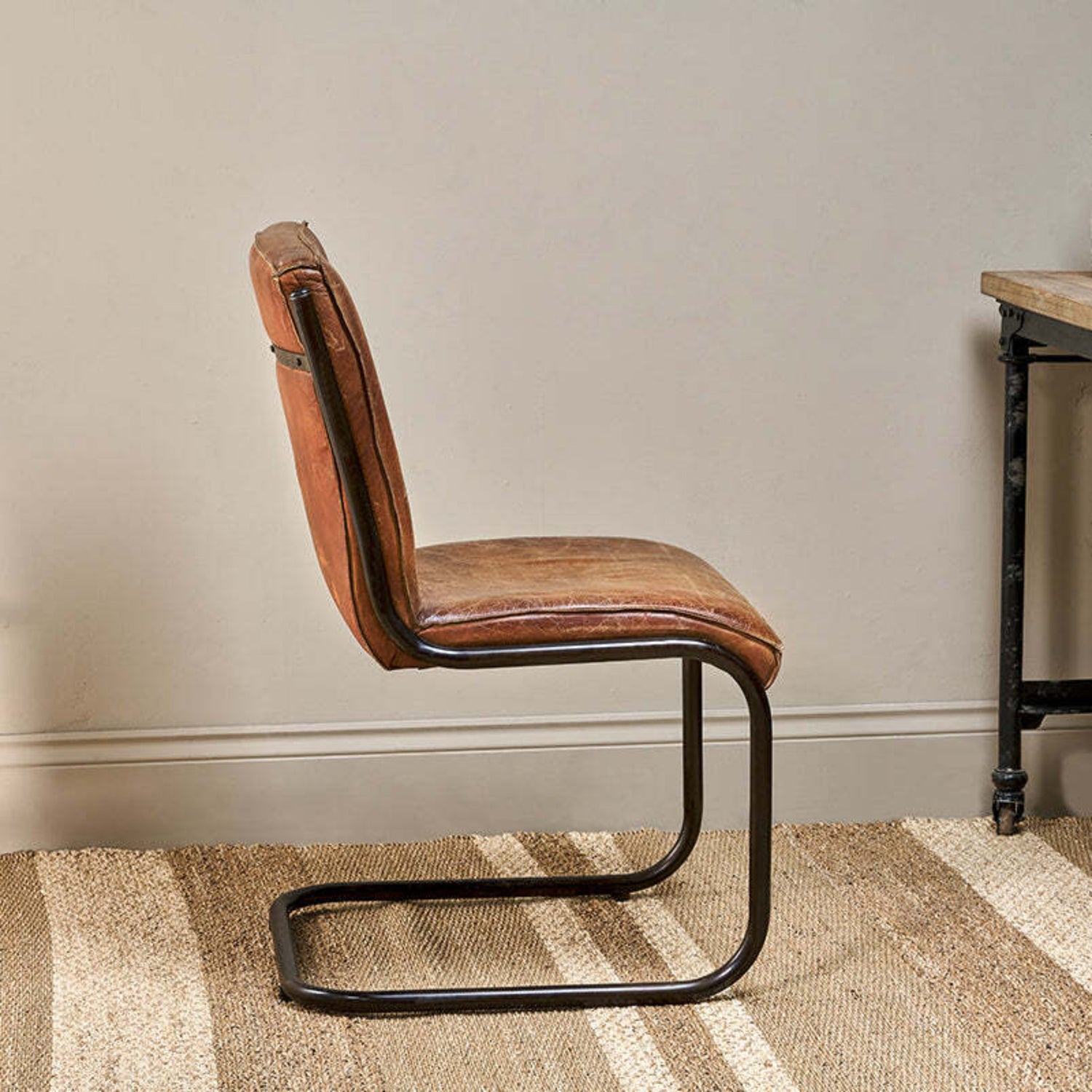 Brown leather chair with metal frame on a striped rug against a neutral wall.