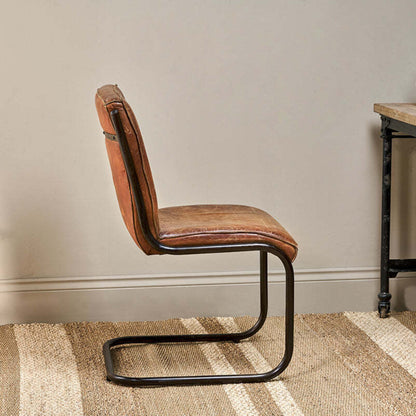 Brown leather chair with metal frame on a striped rug against a neutral wall.