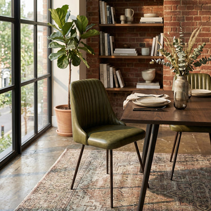 Dining room with a wooden table, green chair, and bookshelf against a brick wall.