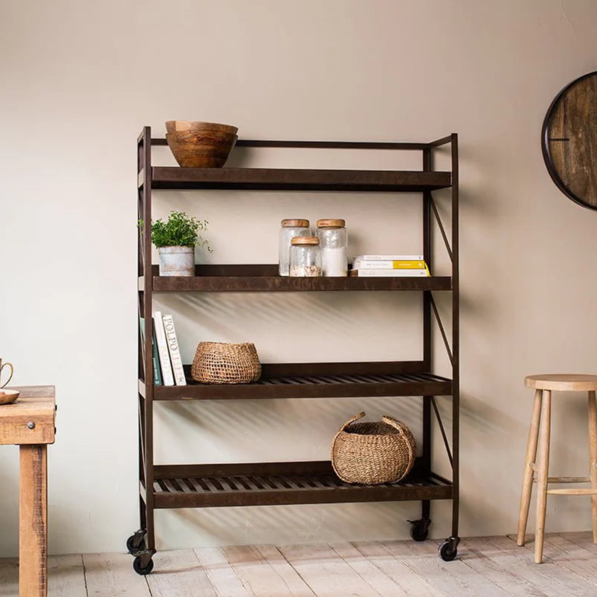 Wooden rolling cart with shelves in a room with a wooden table, stool, and wall clock.