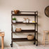 Wooden rolling cart with shelves in a room with a wooden table, stool, and wall clock.