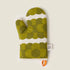 Green patterned oven mitt with a white label on a beige background