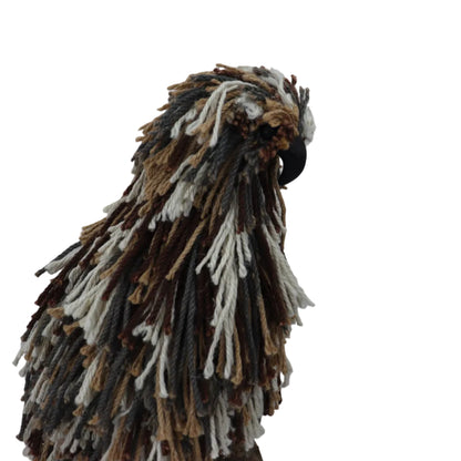 A decorative bird sculpture or bust made from shaggy, frizzy yarn and rope textures in brown, beige, gray, and off-white, with a small black beak, shown against a plain light gray background.