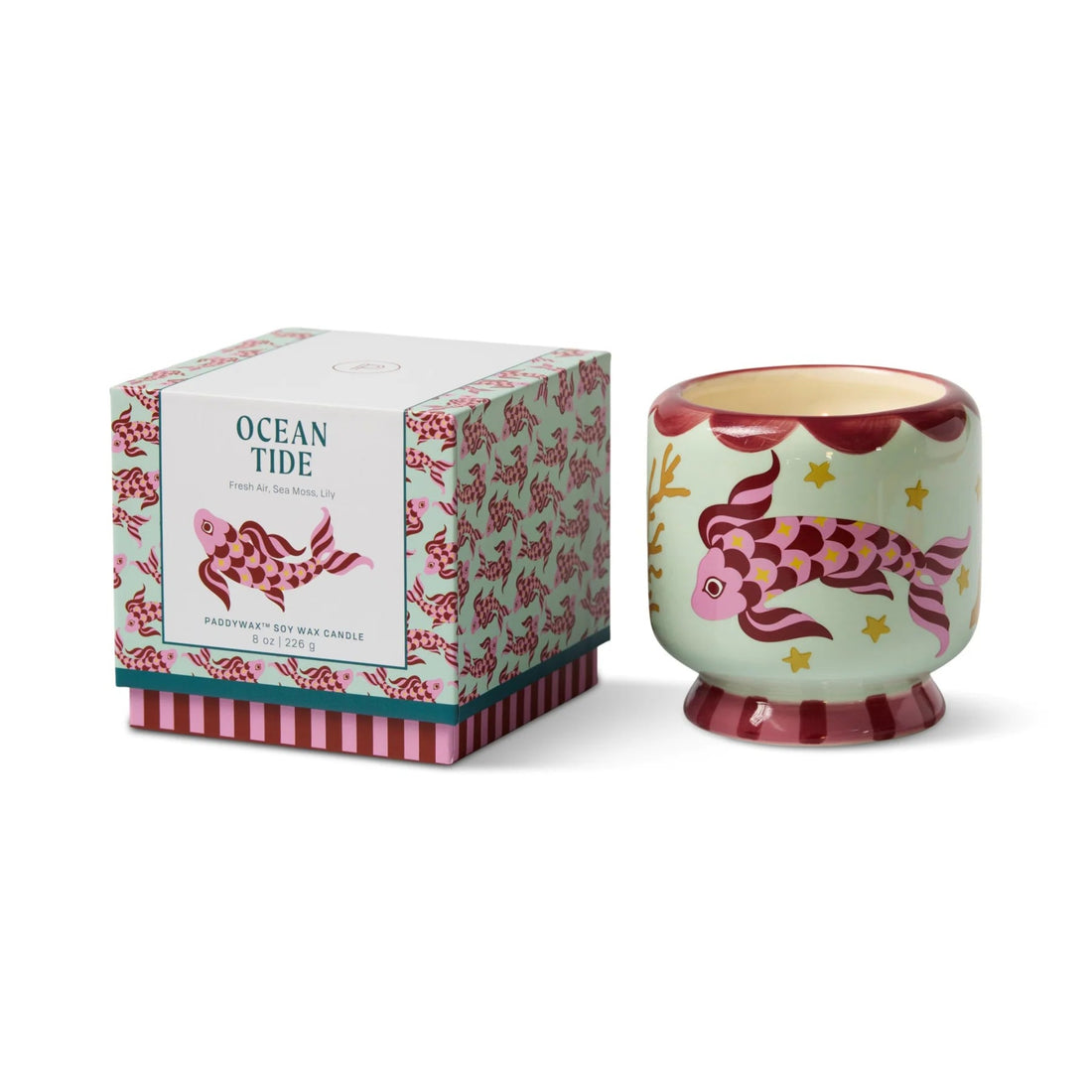 Decorative candle with fish design next to its packaging on a white background