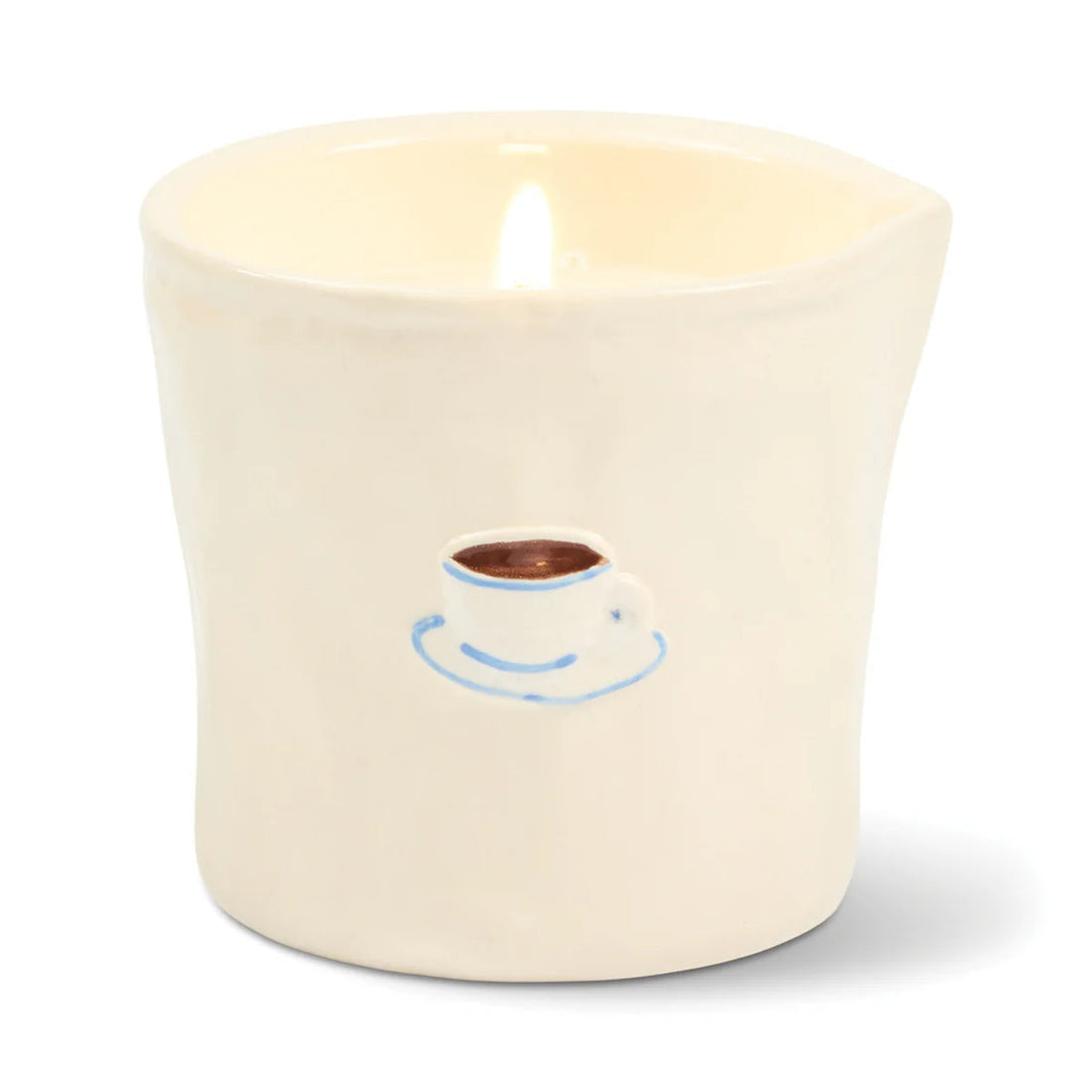 A lit cream-colored ceramic candle holder shaped like a cup with a small blue and brown coffee cup graphic on the front, set against a plain white background.