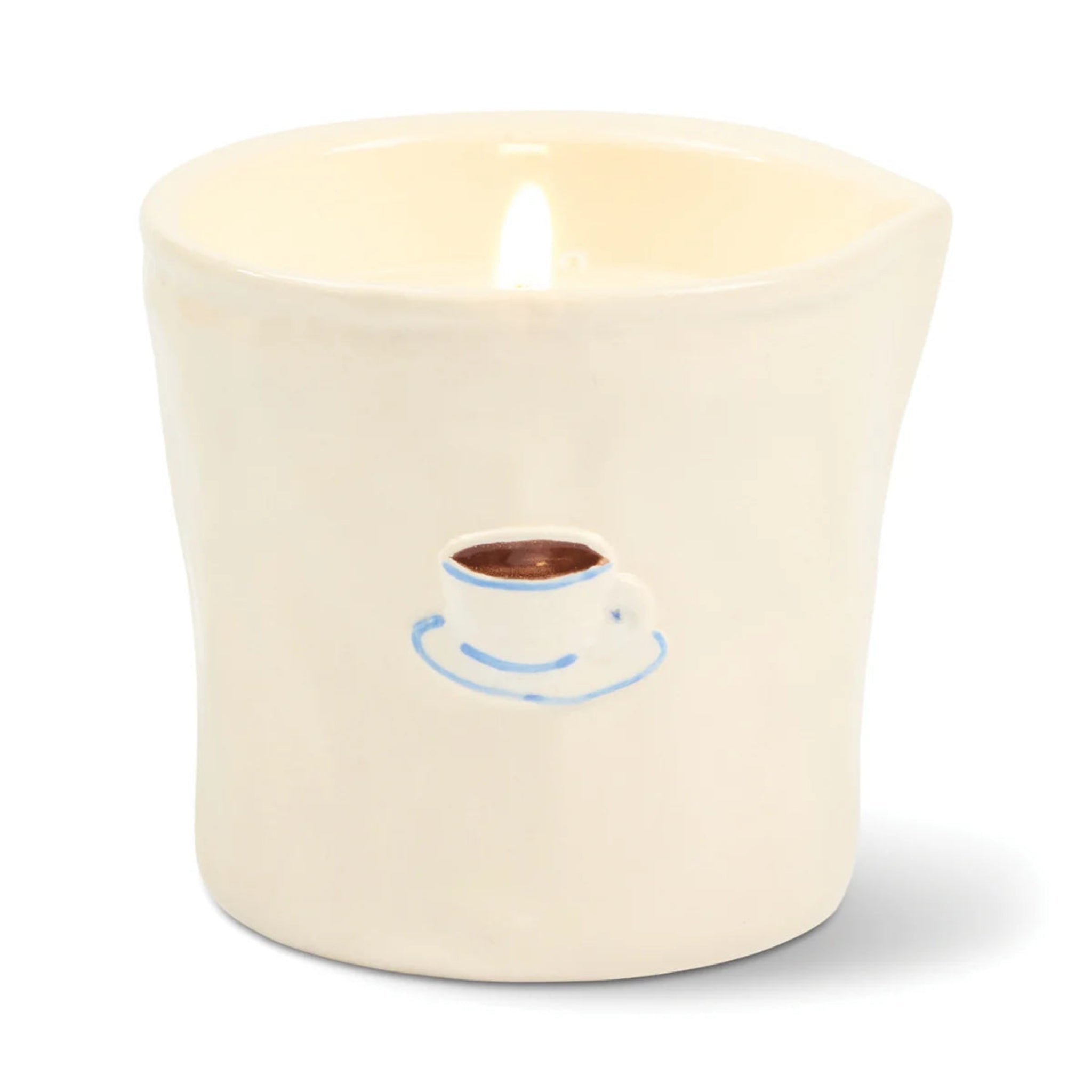 A lit cream-colored ceramic candle holder shaped like a cup with a small blue and brown coffee cup graphic on the front, set against a plain white background.