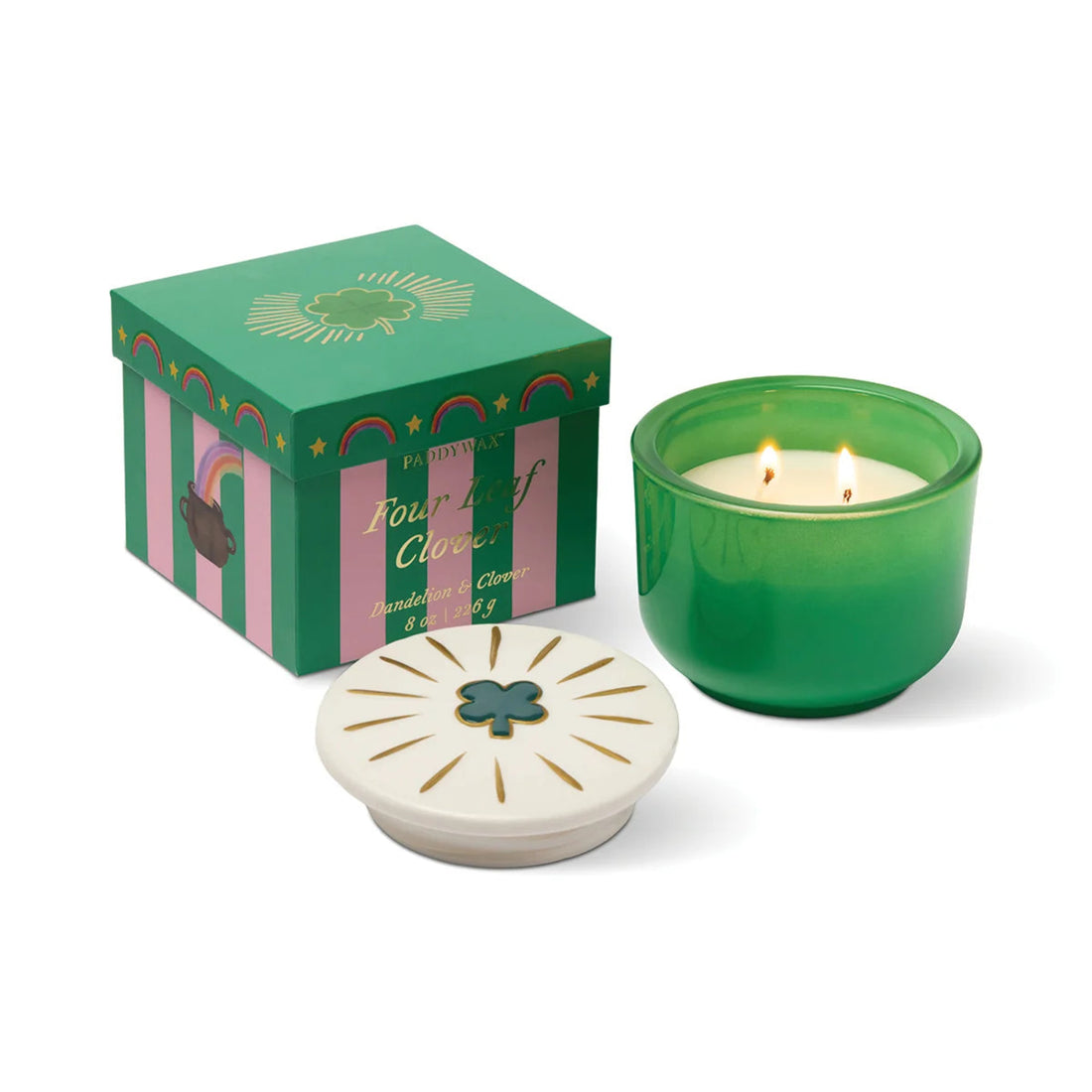 A green glass candle jar with two lit wicks sits beside its decorative green and pink gift box and a white lid featuring a green clover emblem, on a clean white background.