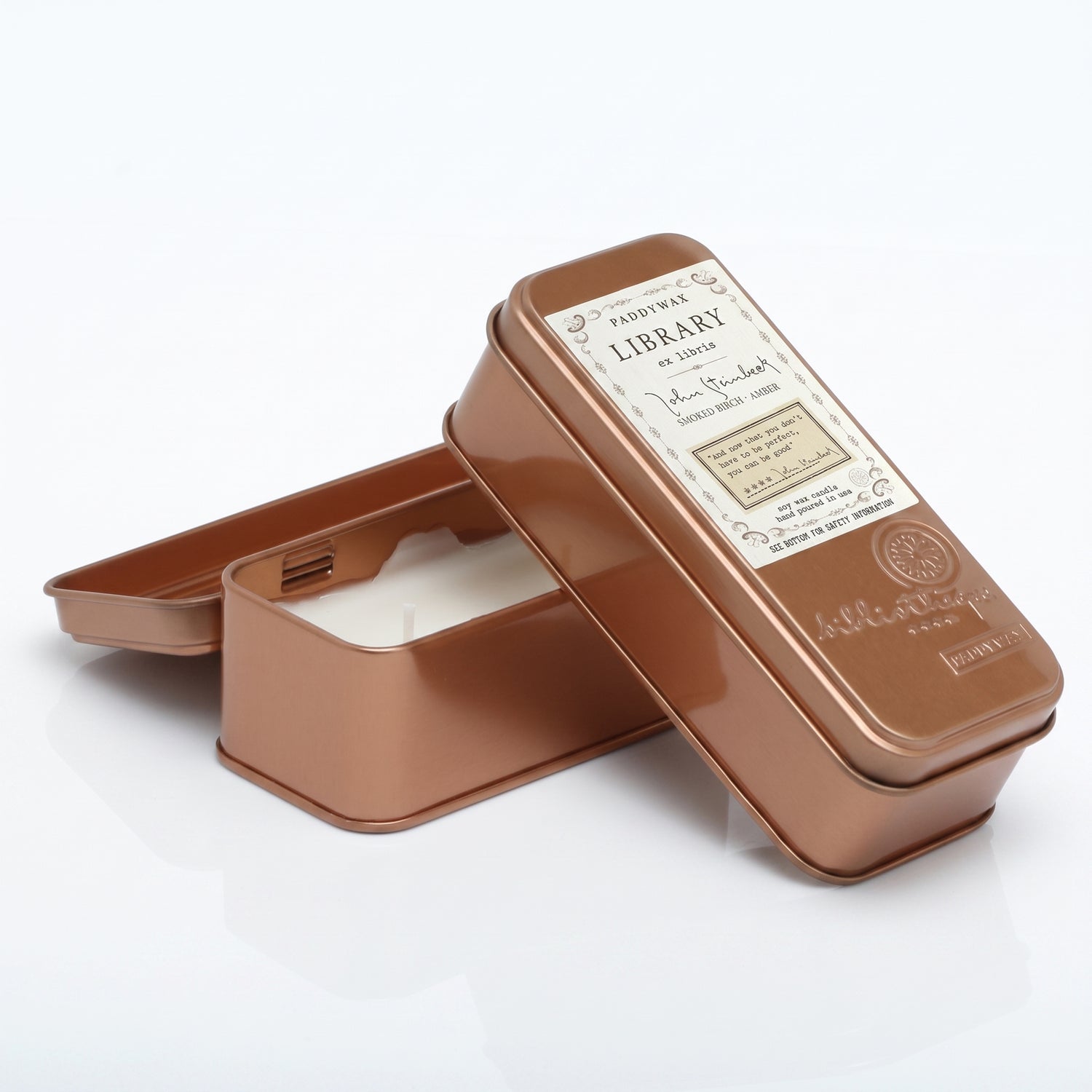 A rectangular metal tin candle shown open with the lid leaning against it on a clean white background. The tin has a warm metallic copper/rose-gold finish and a vintage-style label on the lid reading &