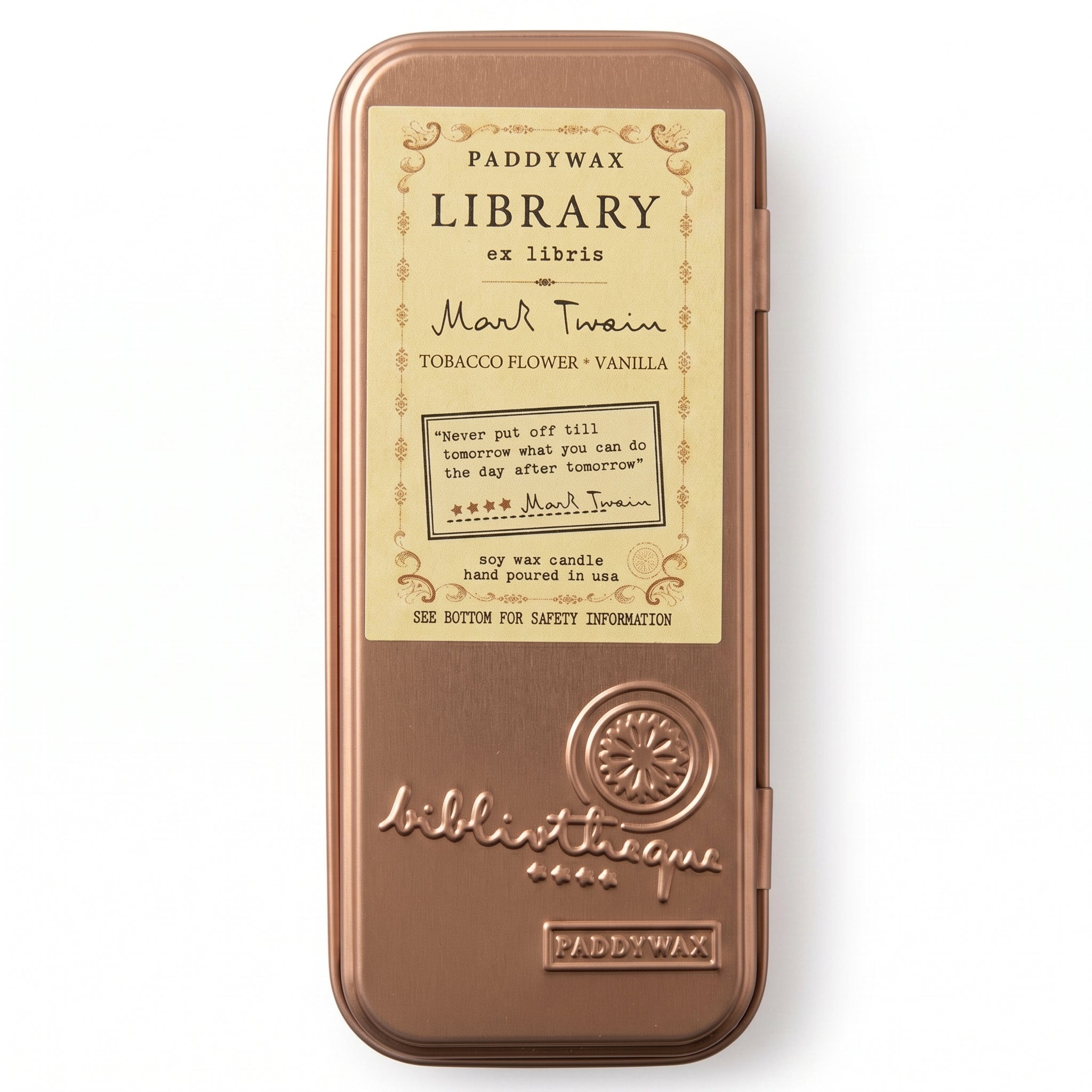 A rectangular metal tin of Paddywax Library ex Libris top wax candle, featuring a warm copper-bronze finish and a cream-colored label with black text. The label details the scent as &