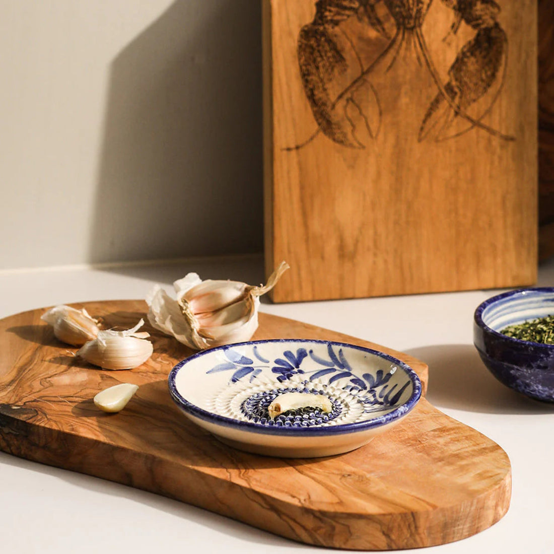 Decorative ceramic bowl with blue patterns on a wooden cutting board with garlic bulbs.