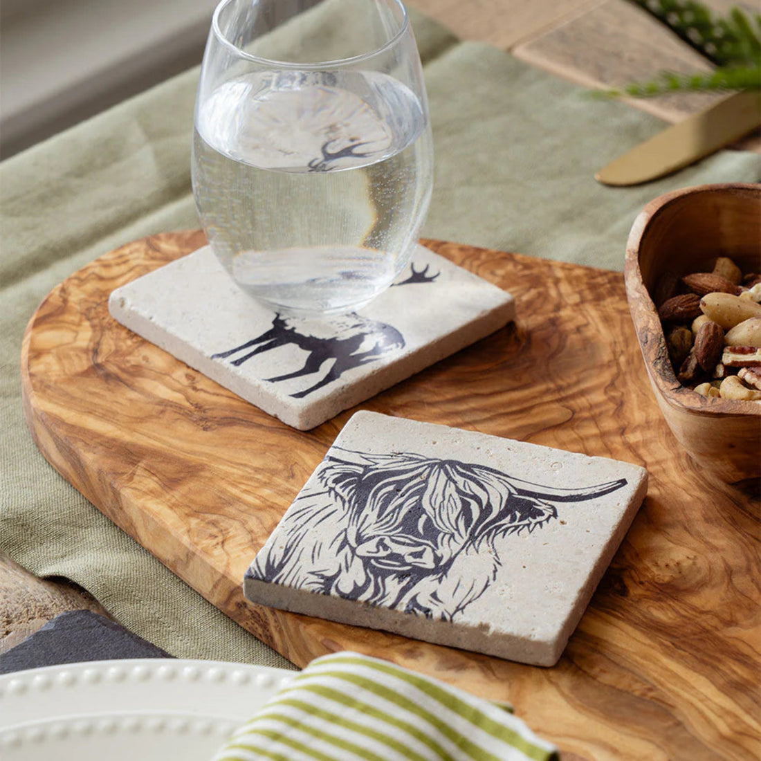 Two stone coasters with animal designs on a wooden tray with a glass of water.