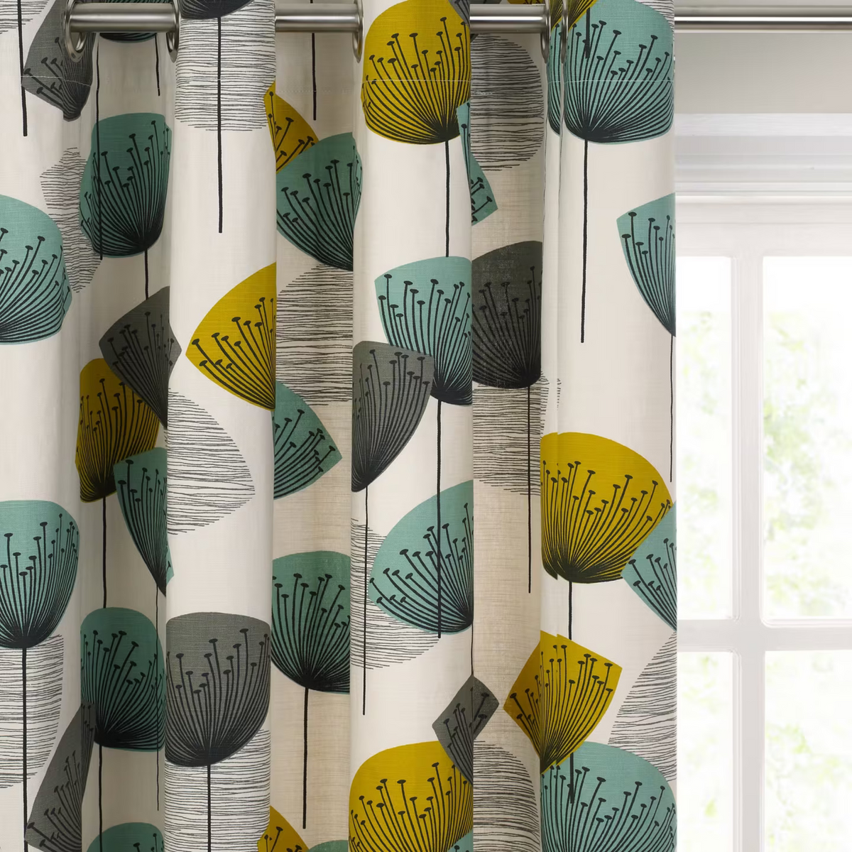 A close-up of patterned curtain panels hanging in front of a bright window. The fabric has an off-white background with a mid-century modern botanical design featuring stylized dandelion-like shapes in mustard yellow, teal, and gray, along with black line details.