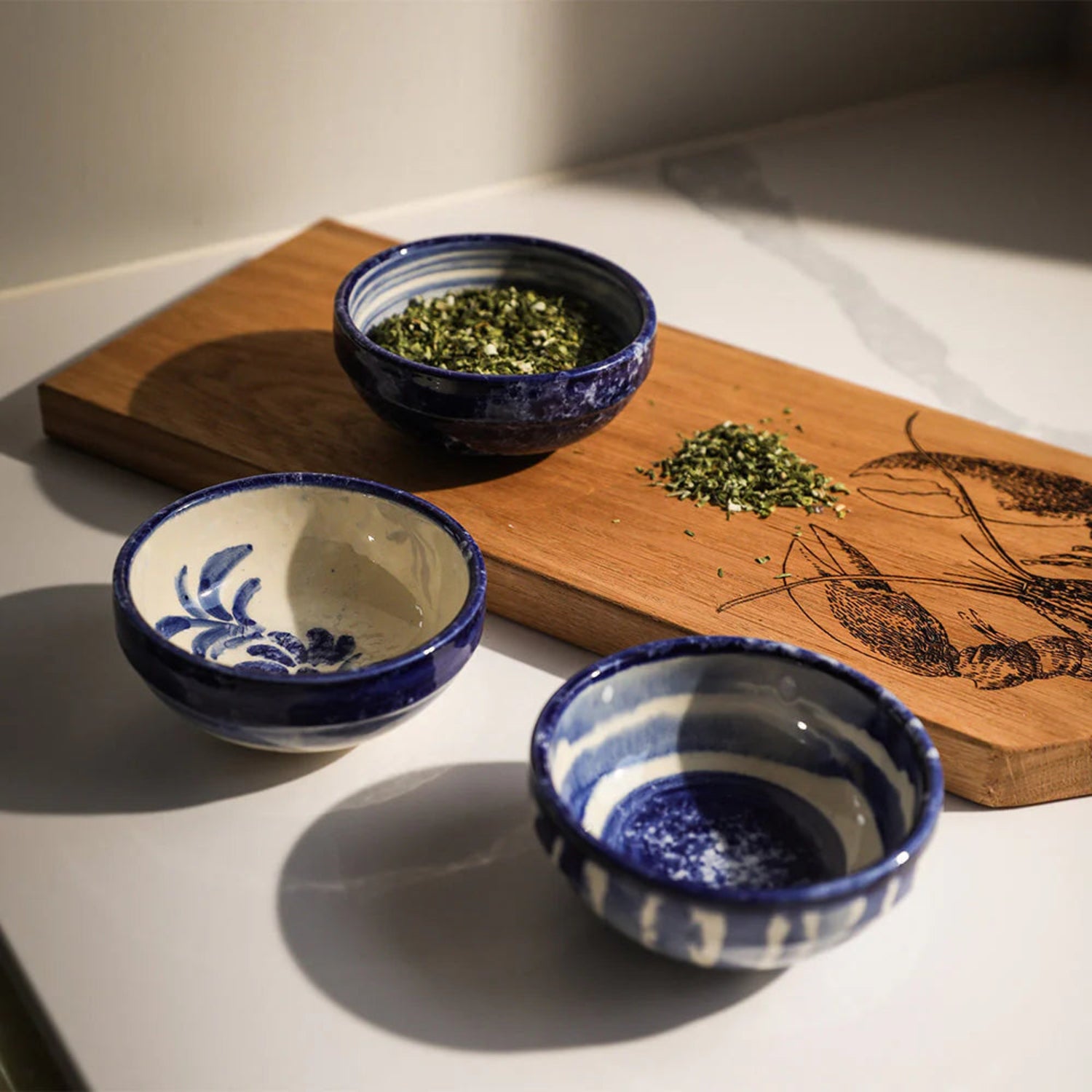 Three blue and white ceramic bowls with green leaves on a wooden board.