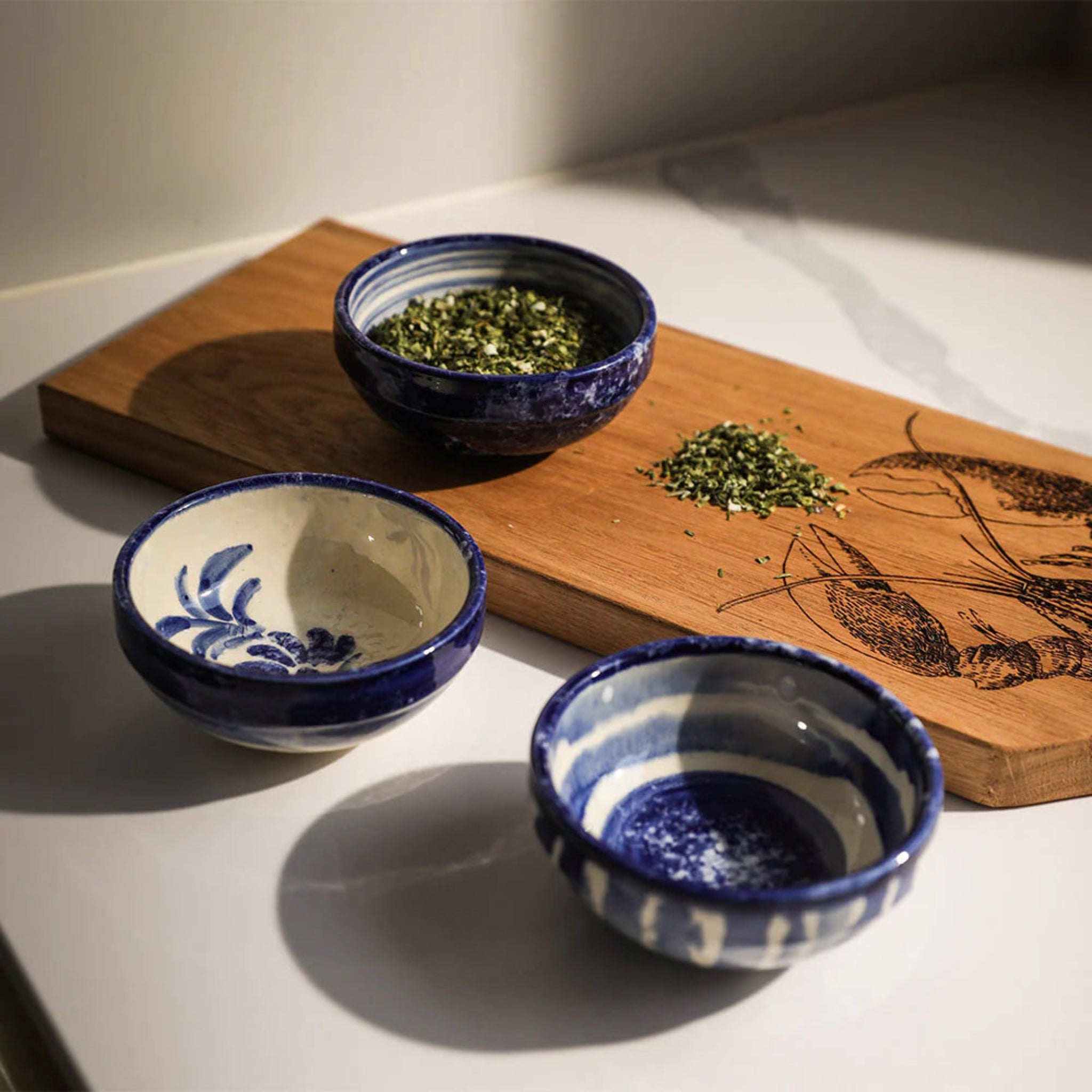 Three blue and white ceramic bowls with green leaves on a wooden board.