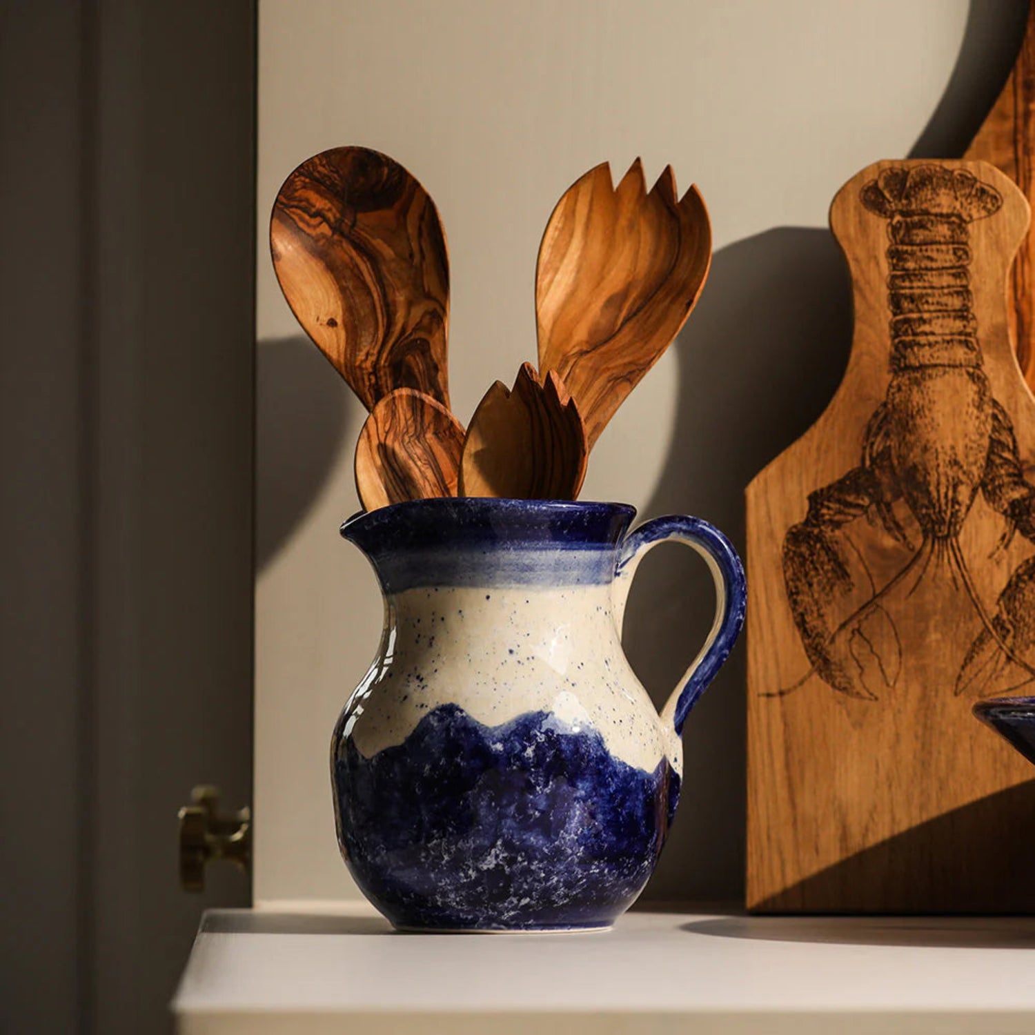 Blue and white ceramic pitcher with wooden utensils on a shelf