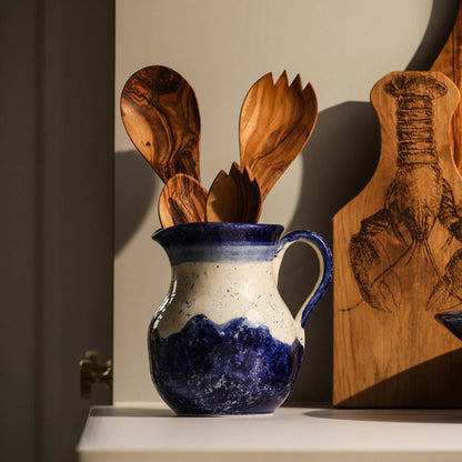 Blue and white ceramic pitcher with wooden utensils on a shelf