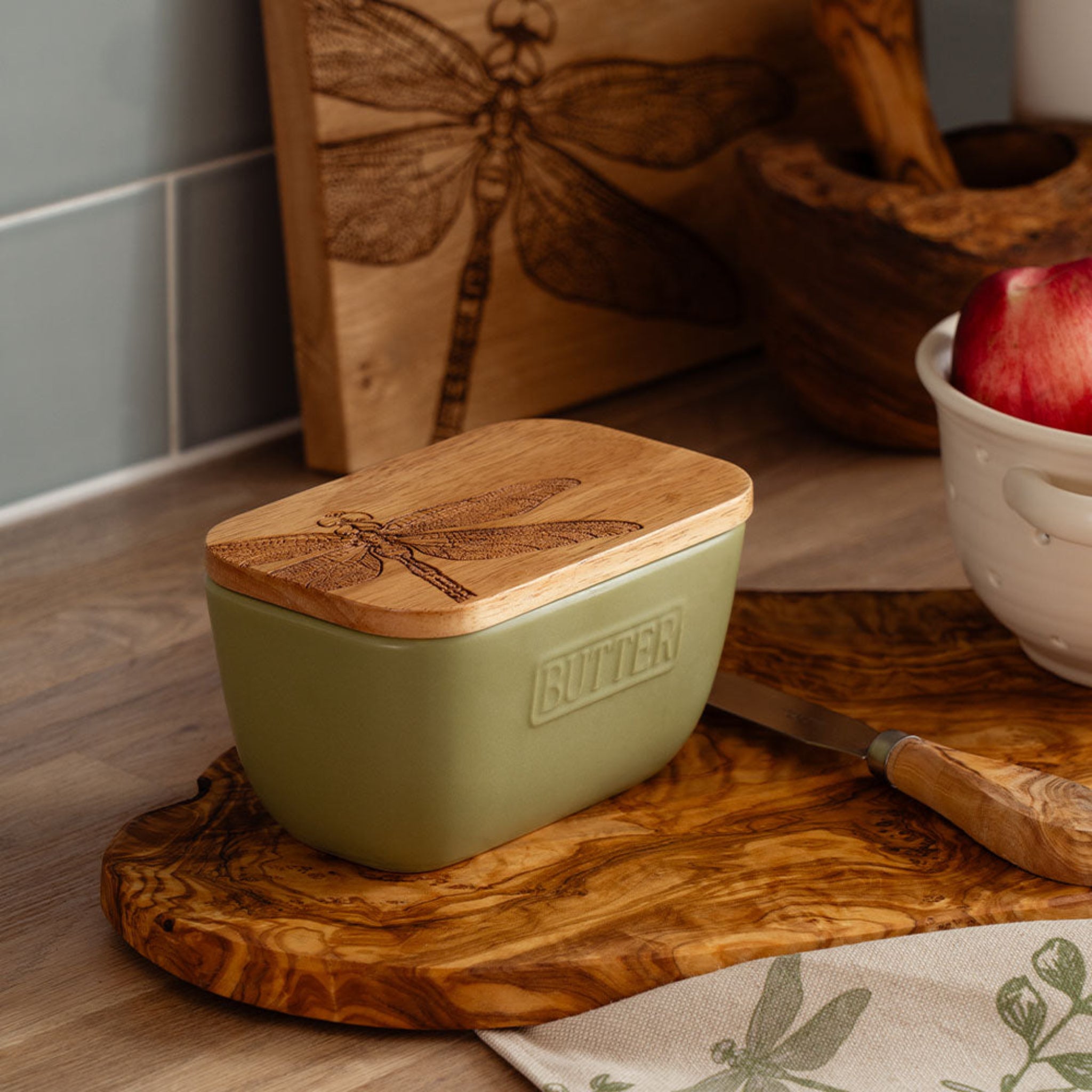 Butter container with wooden lid on a wooden cutting board in a kitchen setting.