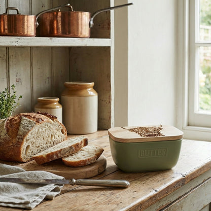Copper pots on a shelf above a wooden table with bread and a green container.