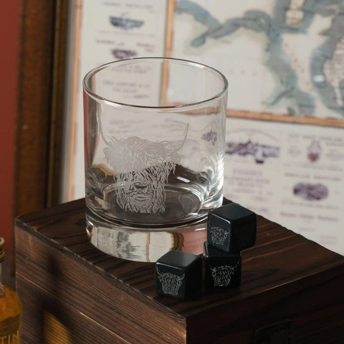 Clear glass with engraved  Highland Cow design on a wooden surface with black stones.