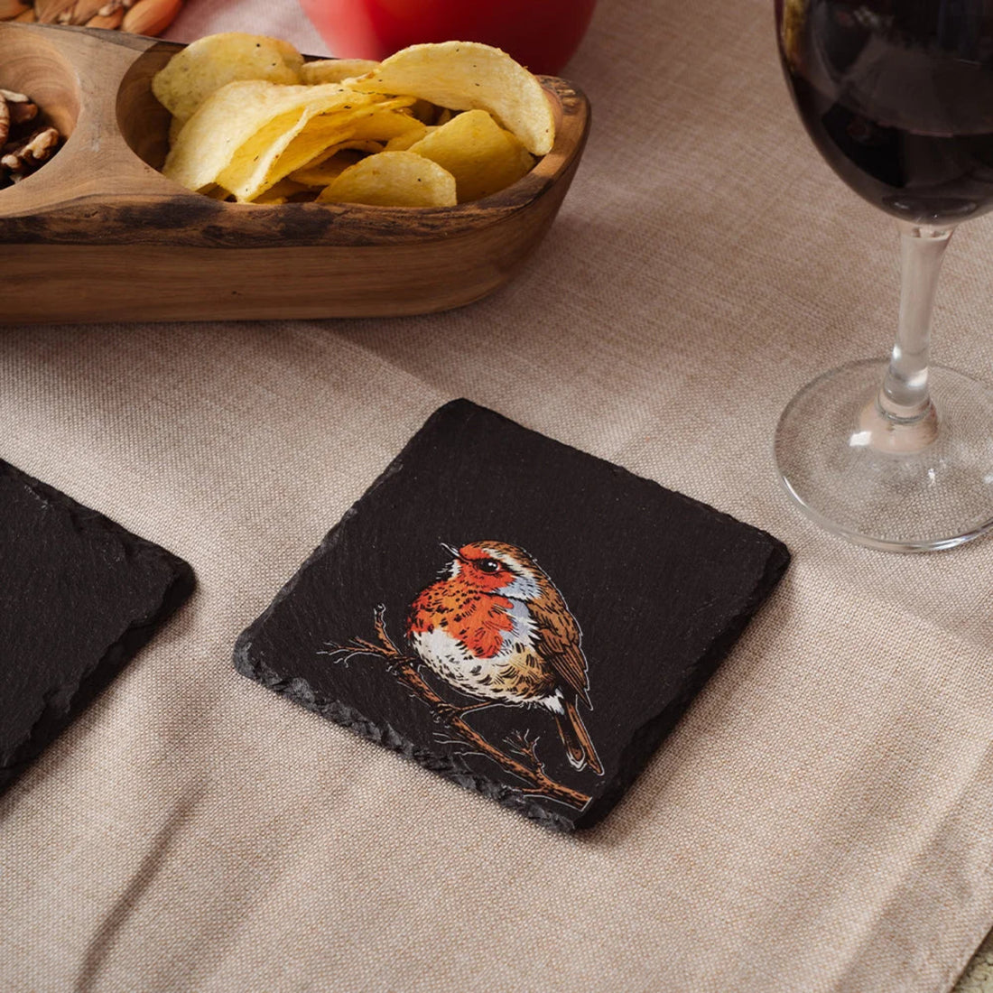 Slate coaster with Robin design on a table with chips and wine