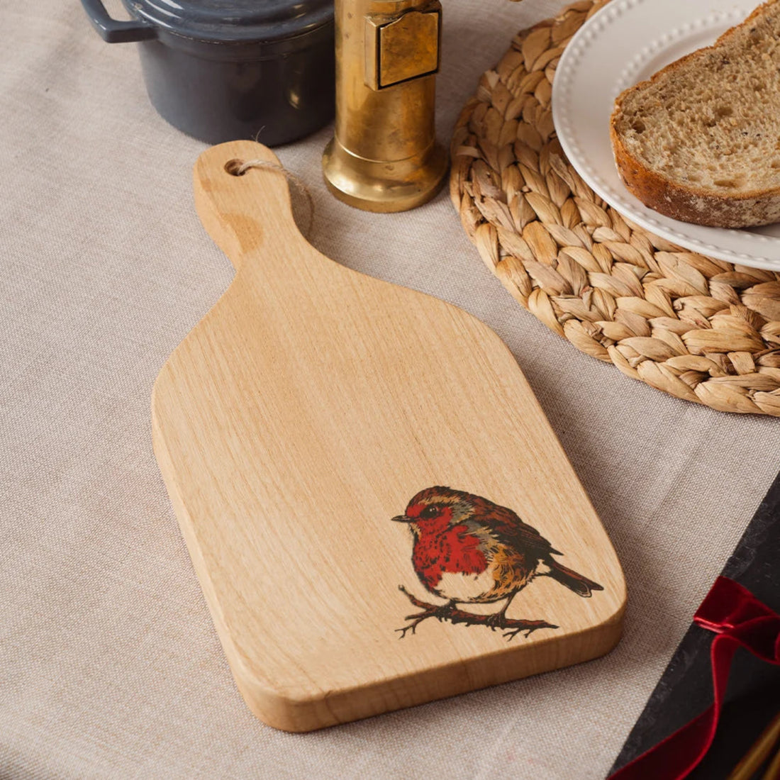 Wooden cutting board with a robin design on a beige surface with bread and a candle.