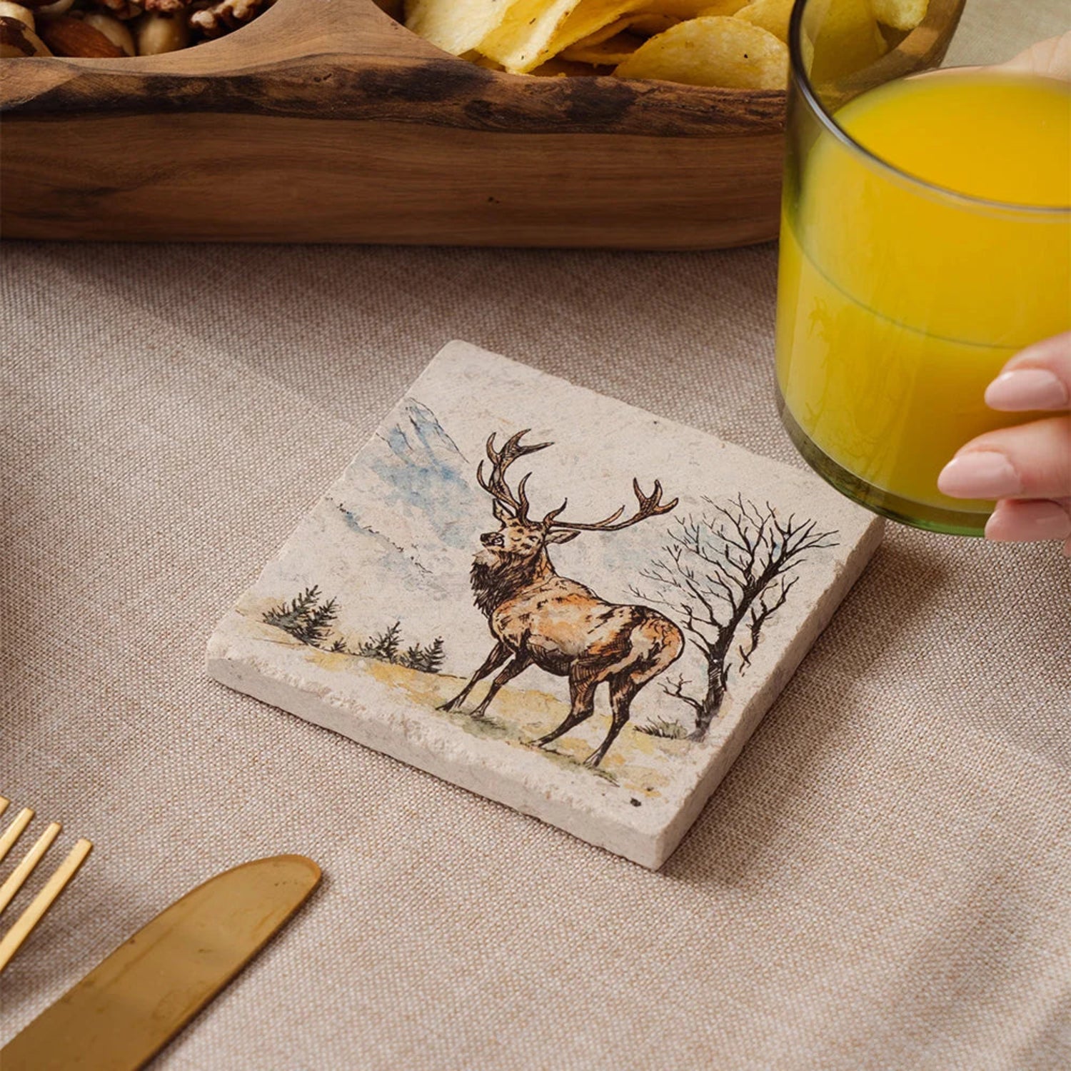 Coaster with deer design on a table with a glass of orange juice.