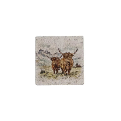 A square stone coaster featuring an illustration of two Highland cows in a grassy field with mountains in the background, shown on a plain white background.