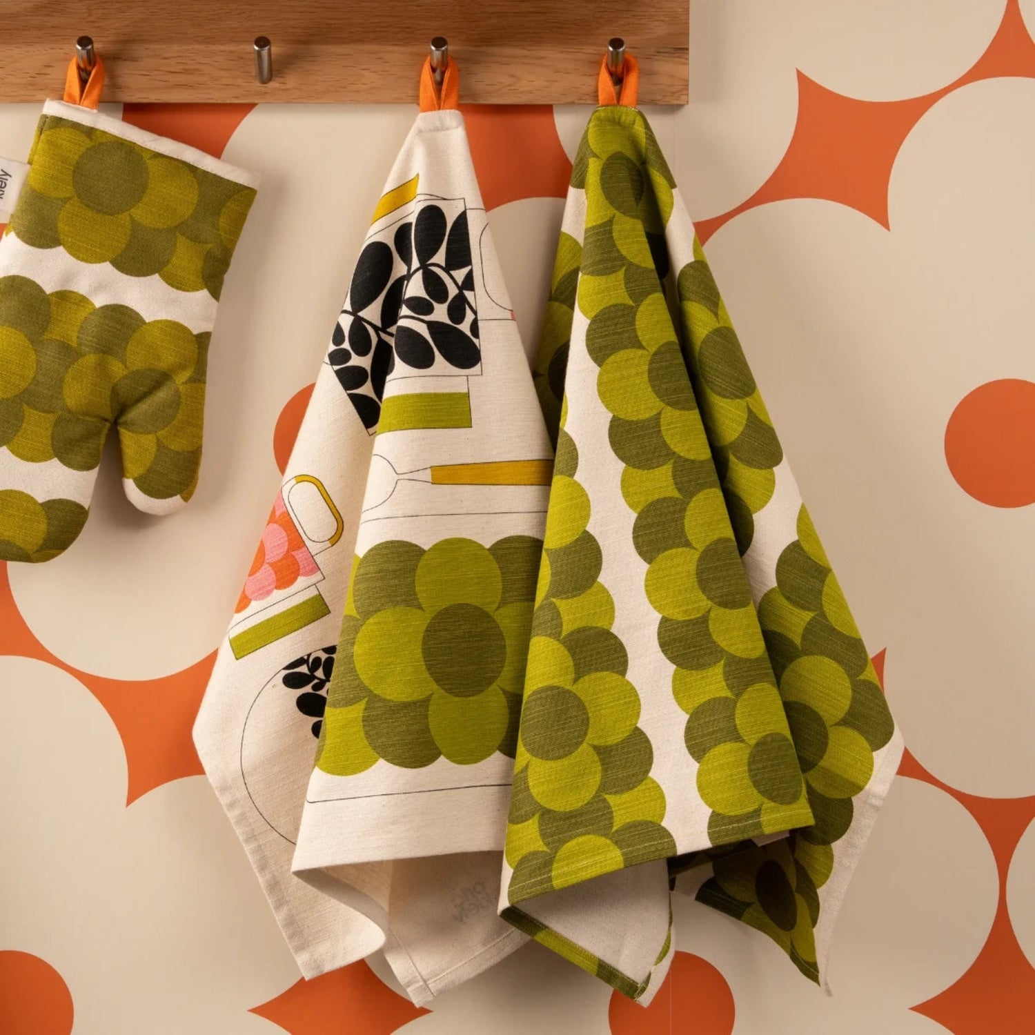 Set of patterned towels hanging on a wooden rack against a geometric patterned wall.
