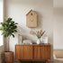 Wooden cuckoo clock on a wall above a wooden cabinet with decor items.