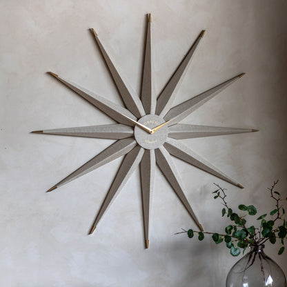 Decorative wall clock with starburst design on a light wall, accompanied by a vase with greenery.