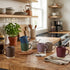 Colorful mugs on a kitchen counter with shelves and appliances in the background