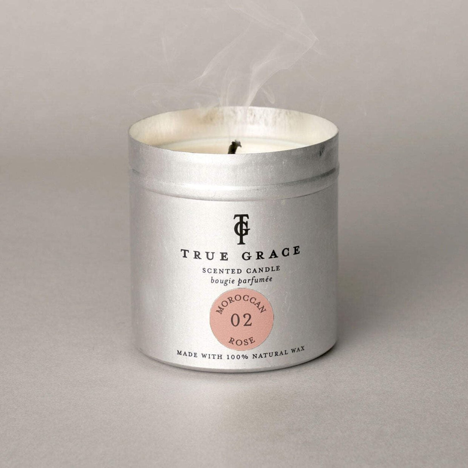 True Grace scented candle in a metallic container on a gray background
