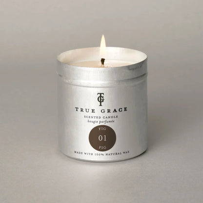 A lit True Grace scented candle in a silver metal tin with a white wax fill, set against a neutral gray background.