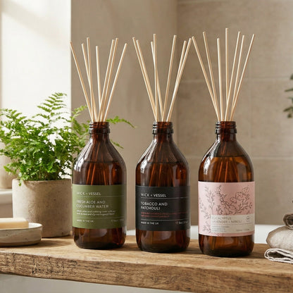 Three diffuser bottles on a wooden surface with plants and towels in the background