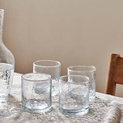 Clear glass carafe and tumblers on a table with a wooden chair in the background.