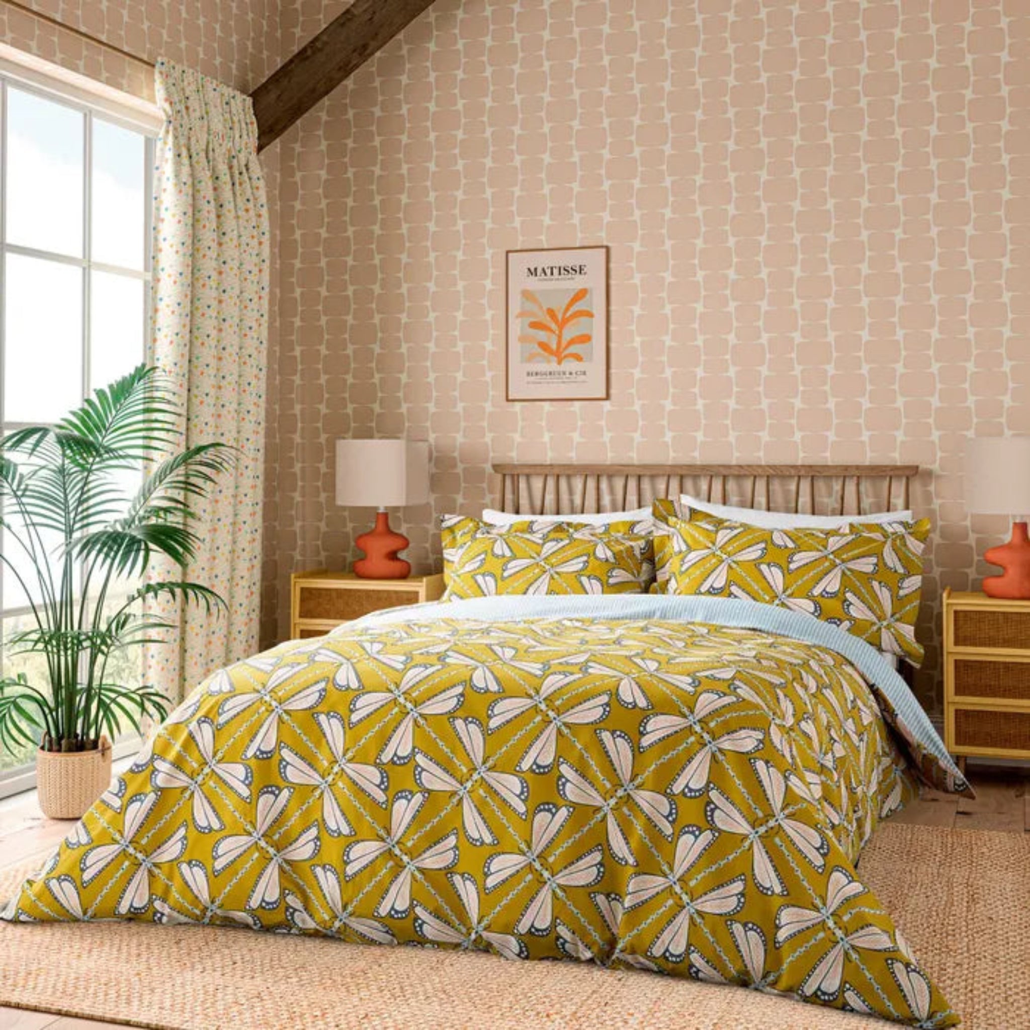 Bedroom with yellow and white patterned bedding, side tables, and a plant.