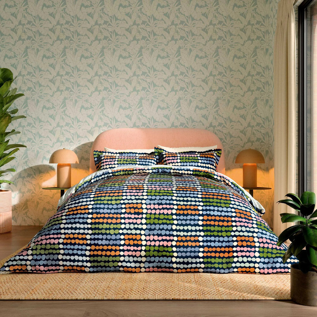 Bedroom with a colorful geometric patterned comforter on a bed, light green walls, and plants.