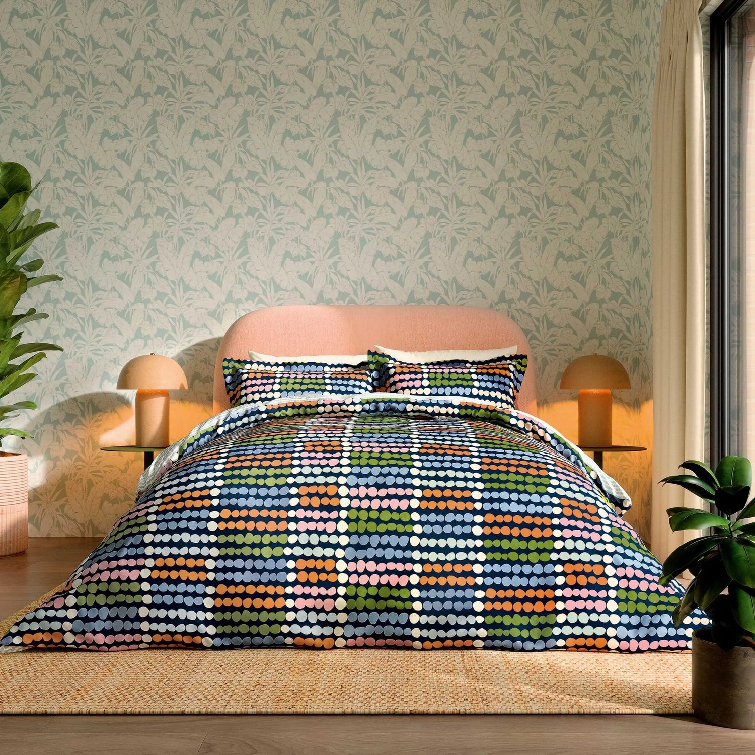 Bedroom with a colorful geometric patterned comforter on a bed, light green walls, and plants.