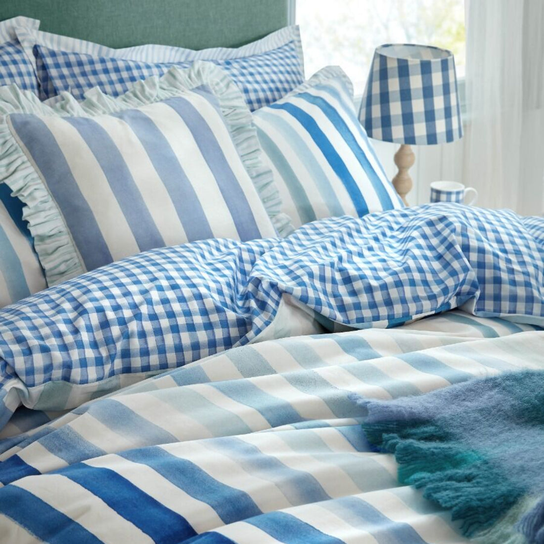 Bed with blue and white checkered and striped bedding, pillows, and a lamp.