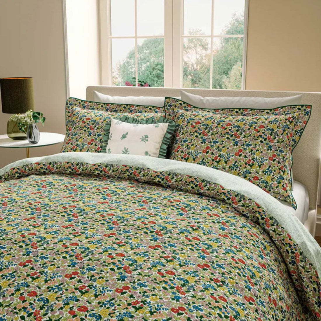 Floral bedding set on a bed with a lamp and window in the background